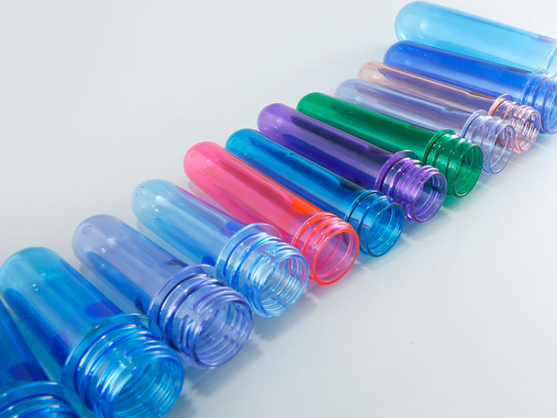 Colorful plastic preforms (blue, pink, purple, green, etc.) arranged in a row on a light background.