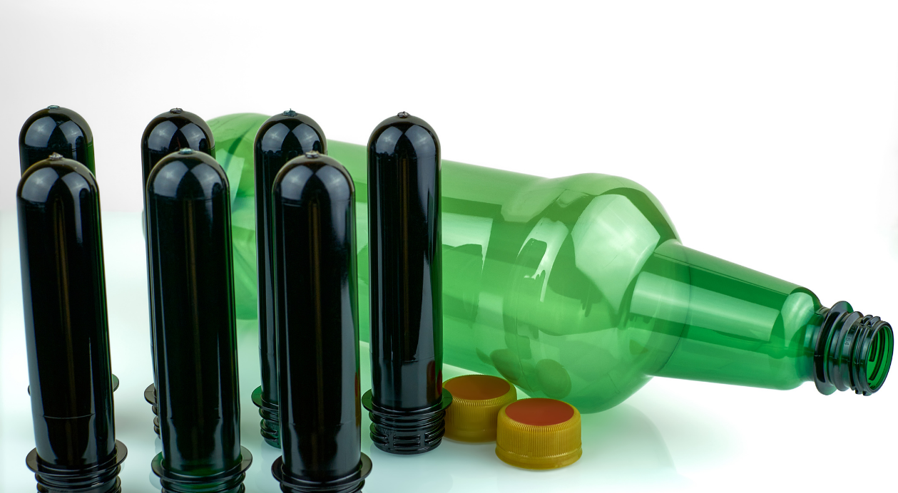 Black PET preforms and a green PET bottle with yellow caps nearby.