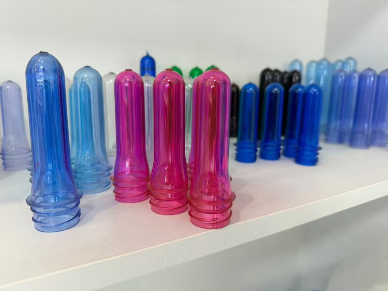 Colorful PET preforms in blue, pink, and other hues displayed on a white shelf.