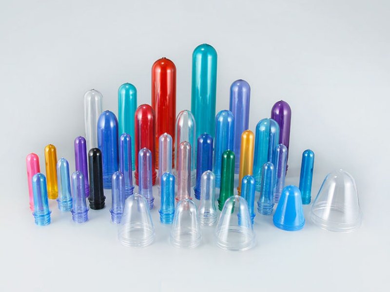 Assorted colorful PET preforms in red, blue, green, and more, arranged on a light background.