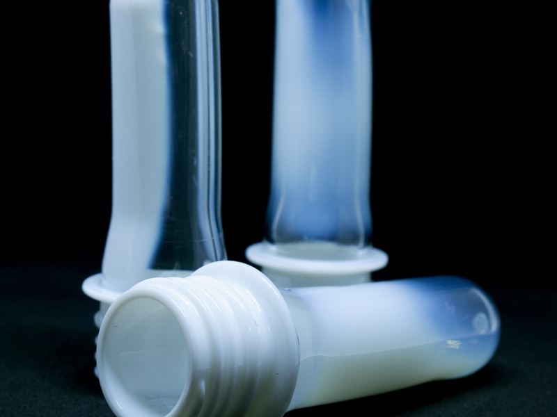 Translucent white PET preforms with threaded necks, placed against a dark background.