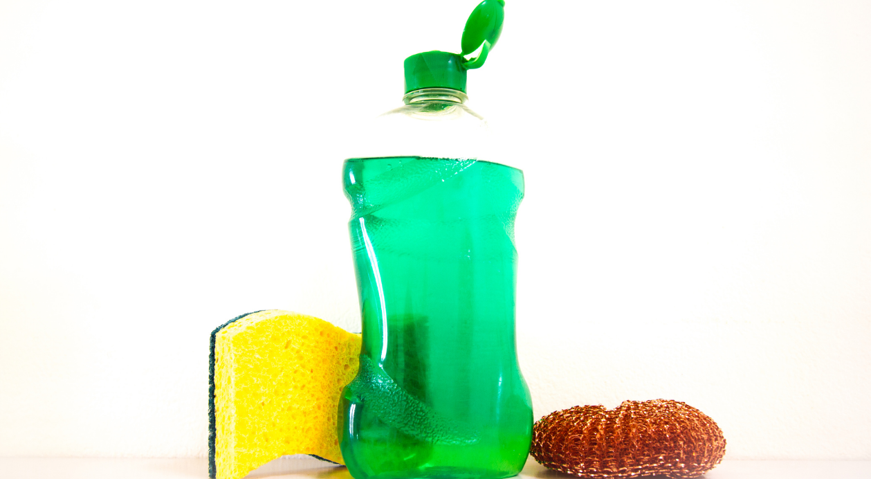 Green liquid - filled PET bottle with a green cap, alongside a yellow sponge and a copper scrubber.